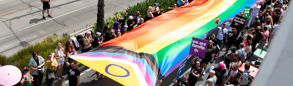 People marching with large rainbow pride flag parade