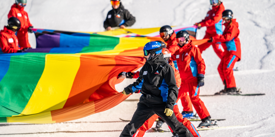 Skiers holding large rainbow flag on snowy slope