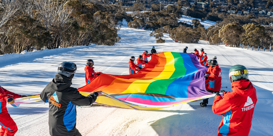 Skiers holding large rainbow flag on snowy slope