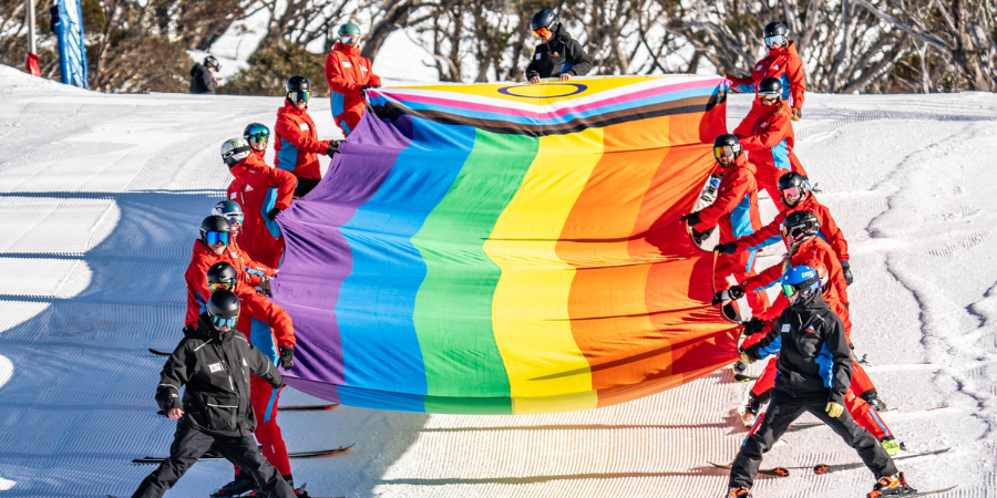 Skiers holding rainbow pride flag on snowy slope