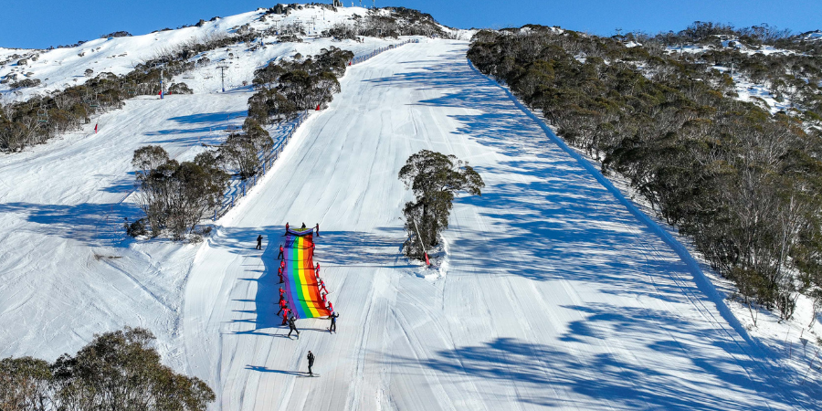 Skiers holding rainbow flag on snowy mountain slope