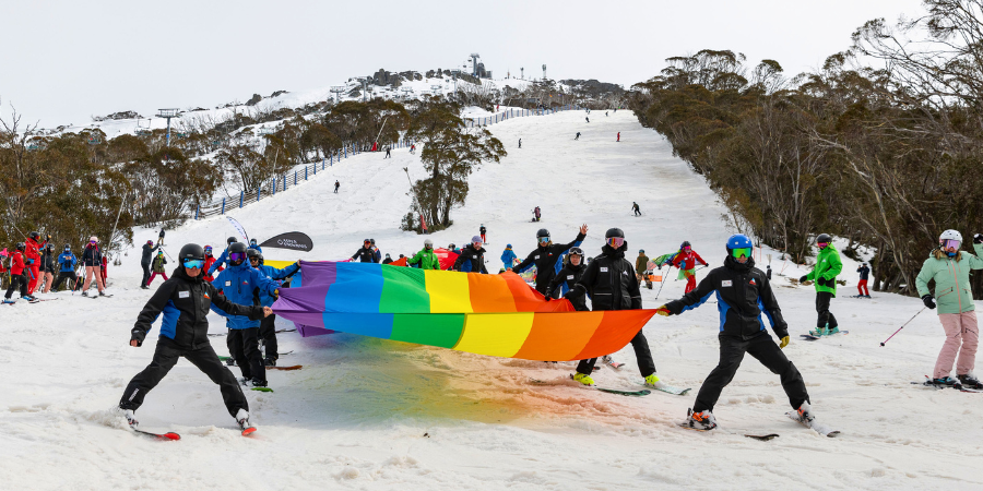 Skiers holding rainbow flag on snowy mountain slope